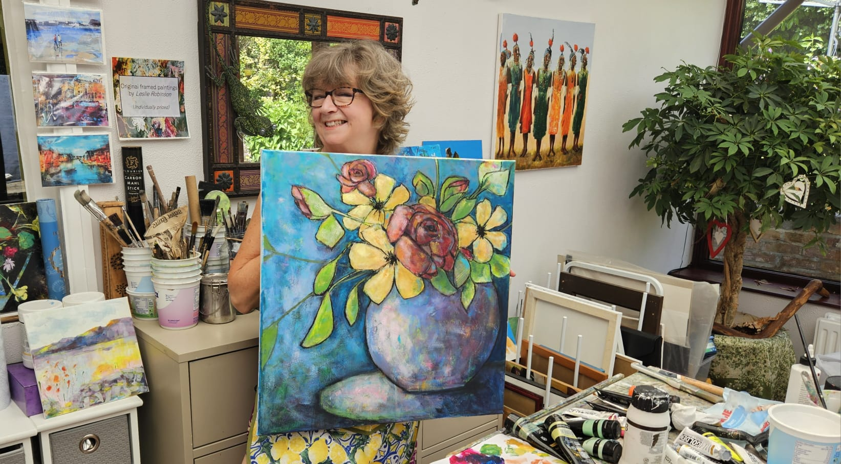 Leslie Robinson holding a finished floral painting in her studio